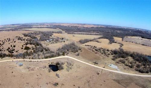 Aerial view of 7.59-acre Cowboy Meadows property in Chautauqua County, Kansas, featuring a pond, open land, and nearby utility access.