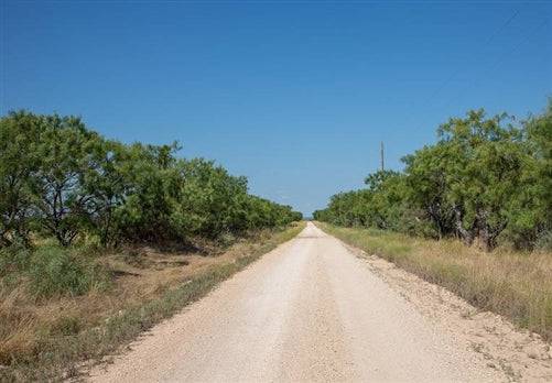 A scenic view of Texas McCulloch County Hunters Ranch Lot 7 showing open land with some trees and electrical infrastructure in the background.